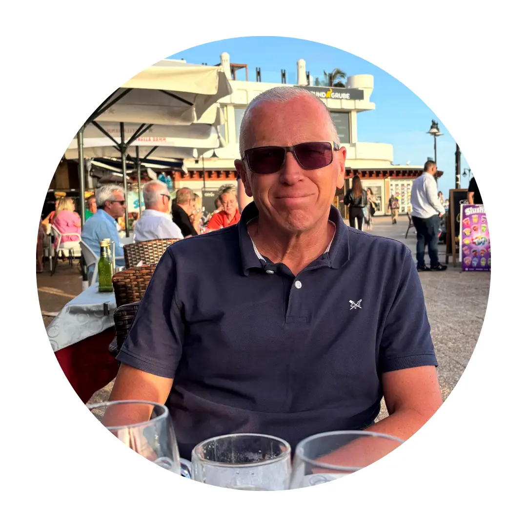 Andrew Boozer smiling at the camera, sitting by the seaside