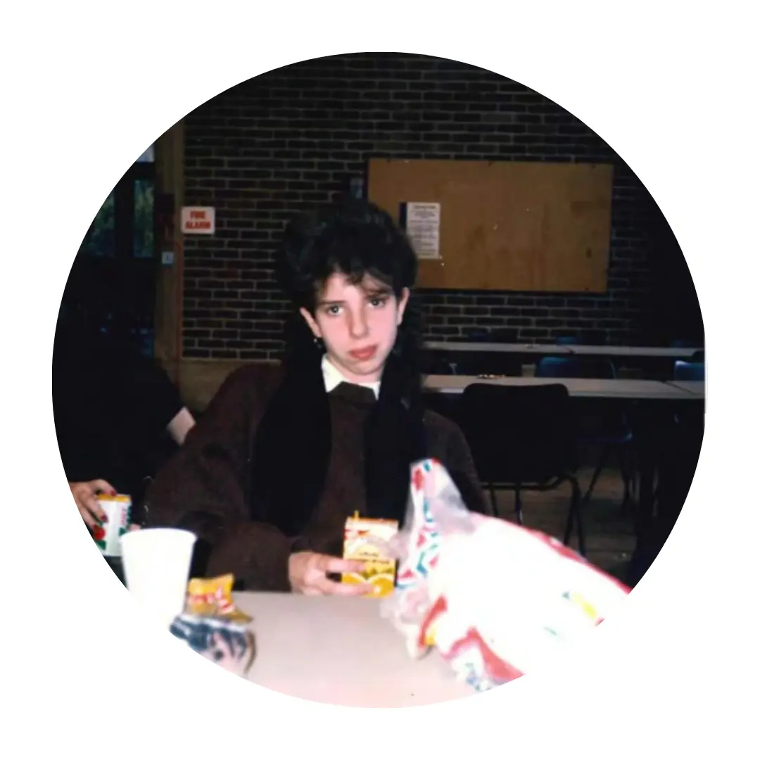Pictured Corrine sitting at a table indoors, holding a small juice box. The background shows a brick wall and some tables and chairs.