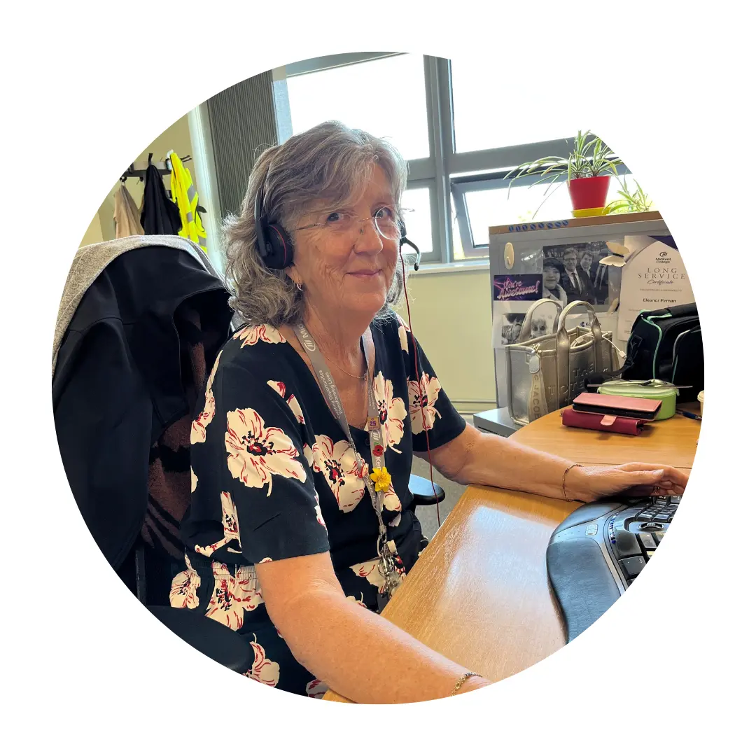 Eleanor Firmin sitting at a desk, wearing a headset whilst working on a computer.