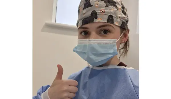 nurse with a face mask and hair net putting her thumbs up to camera