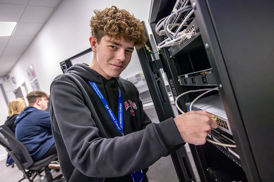 Ethan in an IT room. Smiling at the camera