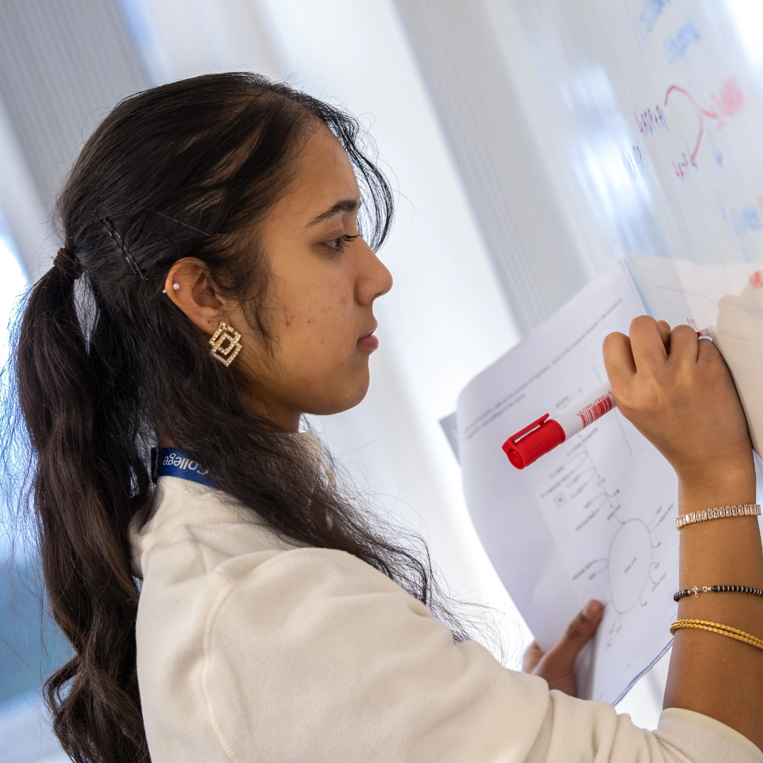 Student writing on white-board in classroom setting
